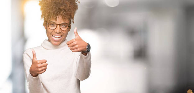美丽的年轻非洲裔美国妇女戴着眼镜，在孤立的背景下，批准用手竖起大拇指做积极的手势，微笑着，为成功而高兴。 看着相机赢家的手势。