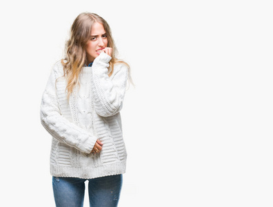 美丽的年轻金发女人穿着冬天的毛衣，在孤立的背景上看起来压力和紧张，双手咬着嘴的指甲。 焦虑问题。