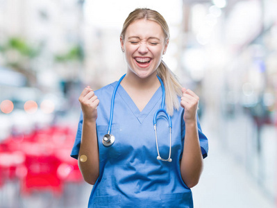 年轻的金发外科医生女医生在孤立的背景下兴奋地成功，举起双臂庆祝胜利，微笑。 赢家概念。