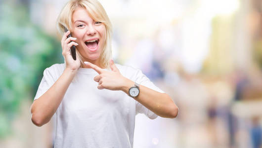 年轻漂亮的金发女人在智能手机上打电话和聊天，在孤立的背景下非常高兴地用手和手指指着。