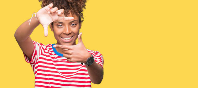 美丽的年轻非洲裔美国妇女在孤立的背景上微笑，用手和手指制作框架，用快乐的脸。 创造力和摄影理念。