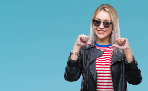 年轻的金发女人穿着时尚夹克和太阳镜,在孤立的背景上看着自信,脸上带