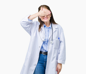 中年成熟的医生女人穿着医用外套，在孤立的背景上微笑和笑，用手捂着眼睛，为惊喜。 盲目的概念。