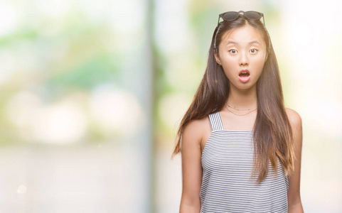 年轻的亚洲女人戴着太阳镜在孤立的背景上害怕和震惊，惊讶的表情，恐惧和兴奋的脸。