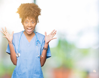 年轻的非洲裔美国医生女士在孤立的背景下庆祝疯狂和惊讶的成功，举起手臂和睁开眼睛尖叫兴奋。赢家概念
