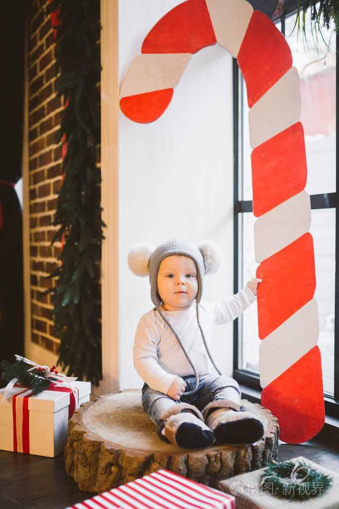 新年和圣诞节主题白种人一岁的孩子坐在窗户附近的一棵树桩上,戴着一