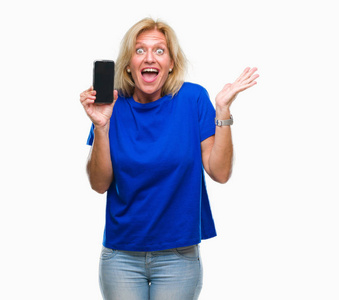 中年金发女性，在孤立的背景下展示着空白的智能手机屏幕，非常高兴和兴奋，胜利者的表情庆祝胜利，微笑着尖叫，举起双手