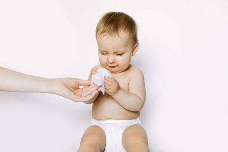 卫生年轻妈妈用湿巾擦拭婴儿皮肤。穿着尿布的小女孩坐着，从妈妈手里拿着湿抹布。清洁擦拭，清洁