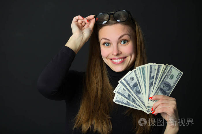 美丽的年轻快乐的女孩,带着惊讶的脸,手里拿着钱在黑色的背景上照片