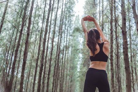 妇女伸展手臂，呼吸新鲜空气在松木森林中间锻炼。 锻炼和生活方式的概念。 幸福生活和医疗保健主题。 自然和户外主题。 背面视图