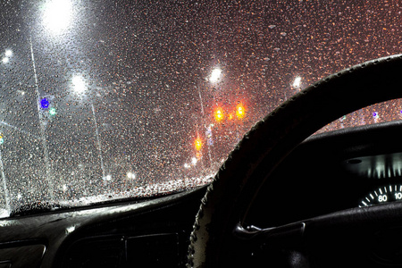 在夜间城市的雷雨和雨中，玻璃清洁剂打开了汽车挡风玻璃上美丽的水滴。 前后背景模糊