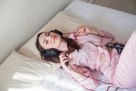 美丽的女人在睡衣听音乐与耳机在床间