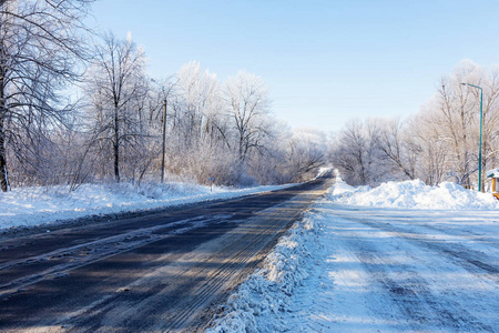 白雪覆盖的冬季道路。 雪覆盖道路一侧霜雪中的树木。 在寒冷阳光明媚的冬日，明亮的雪景