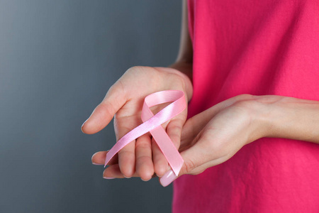 女人拿着粉红色的丝带在灰色背景特写与空间的文本。 乳腺癌意识
