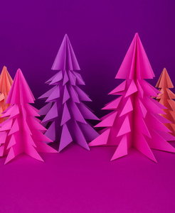 由粉红色和紫色工艺纸制成的圣诞树。 手工艺品。 紫色背景。 森林折纸