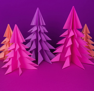由粉红色和紫色工艺纸制成的圣诞树。 手工艺品。 紫色背景。 森林折纸
