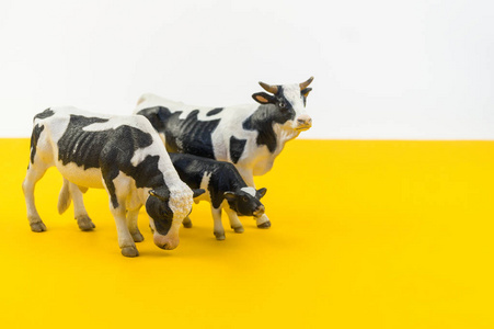 用黄色背景上的塑料制成的玩具牛。 从农场给孩子的动物。 宠物人造动物。