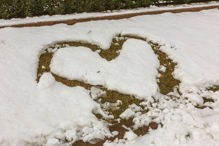 薄春雪中的心符。 心的象征被践踏在薄薄的新鲜雪中，穿过雪的轮廓，矗立在草地上。