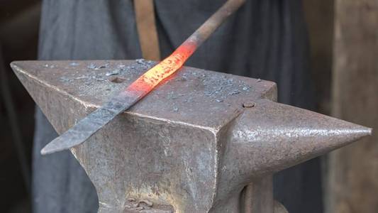 铁匠在铁砧上锻造铁铁匠在铁砧上持有热钢棒用铁匠机器把炽热的红色