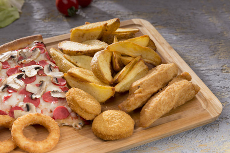 将意大利比萨饼炸洋葱圈土豆和鸡块贴在木切割板上