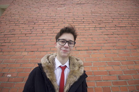 一个穿着毛领外套的年轻人的肖像。 在广角镜头上用扭曲拍摄。 在砖墙的背景上。