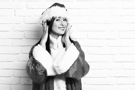 相当可爱的圣诞老人女孩或微笑的黑发女人在红色毛衣与圣诞节或圣诞帽在白色砖墙背景, 复制空间