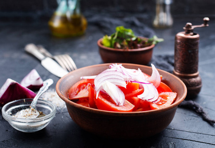 沙拉和新鲜的西红柿和洋葱放在灰桌面的碗里
