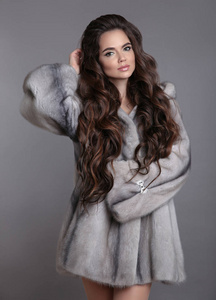 优雅的女人穿着貂皮大衣，孤立在灰色的工作室背景上。 深色的女孩穿着豪华的冬季外套。