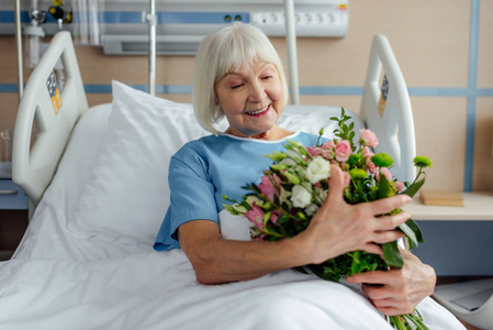 微笑着，正在康复的老年妇女躺在床上，医院里开着花