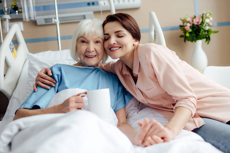 医院床上抱着一杯茶的快乐老太太和女儿