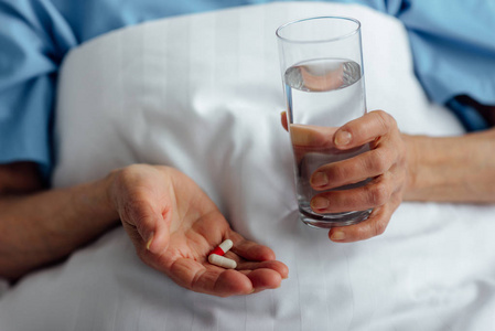 老年妇女躺在床上，在医院里拿着一杯水的药丸