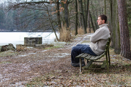 年轻人的肖像坐在穿毛衣的老长凳上。