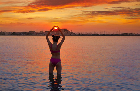 女孩在日落时的剪影，心形在手中，手指在海滩上