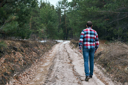 在穿过针叶林时，雄性在肮脏的乡间道路上行走的后景