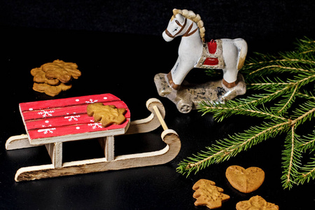 木制雪橇和玩具马与圣诞树树枝和圣诞饼干黑色背景