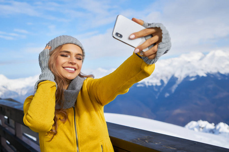女滑雪者在雪山背景下拍摄自拍照片