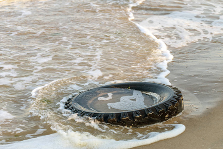 旧黑色橡胶轮胎遗留在沙滩上，环境污染理念，选择性聚焦，色彩调色图片..在海滩上蓝色的水中丢弃的旧轮胎。海洋和海滩上的污染和垃圾