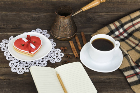 咖啡杯，心形饼干与信息，笔记本，铅笔和咖啡壶在棕色的木桌上。假日计划