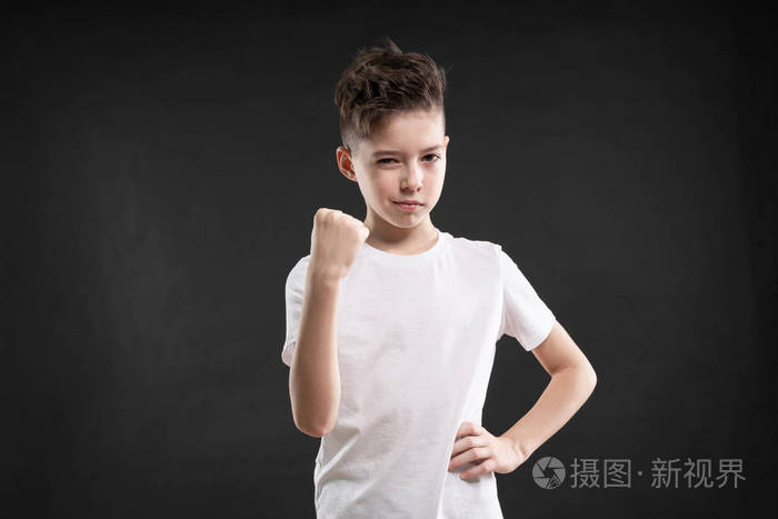 愤怒的白种人男孩在黑色背景上展示拳头的肖像
