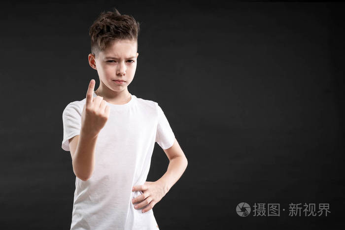 严肃的白种人男孩在黑色背景下做第一个手势的肖像. 小孩指指点点食指