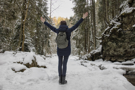 带着背包的女孩站在雪林中举起手臂。 冬天。