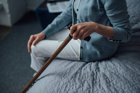 老年妇女坐在床上拿着手杖在家中的剪影