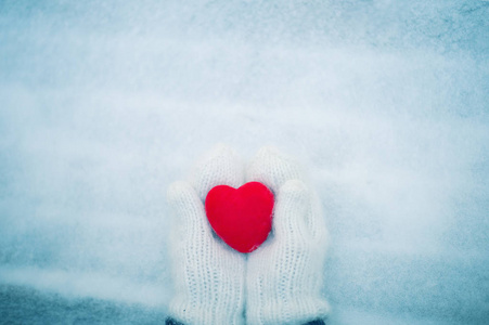 红色的心在女人的手中戴着白色的羊毛手套。情人节概念