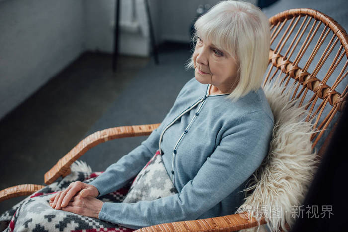 坐在家里的柳条摇椅上的悲伤的老年妇女