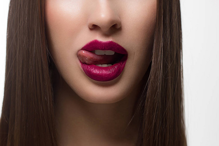 用舌头闭上的女性嘴唇。 干净的皮肤和清晰的嘴唇轮廓被勾勒出一个时尚的玛萨拉口红。 白色牙齿和微笑的美丽，为雄蕊水疗或美容