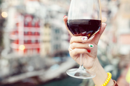 意大利国旗指甲艺术中的女性手拿着酒杯,杯中有红酒,背景是朱克特里