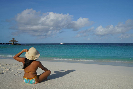 女人戴着帽子坐在阳光下的沙滩上