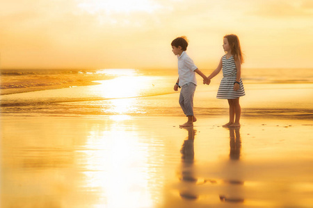 孩子们在夕阳下牵着手在海滩上散步
