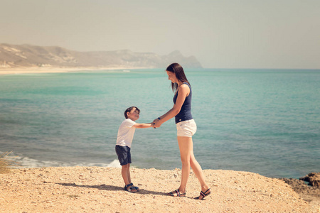 母亲和儿子站在海滩上，双手握着背景上的蓝色海水