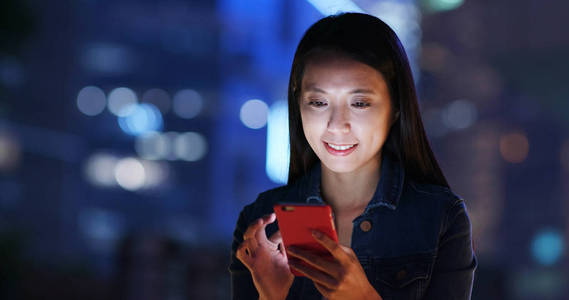 女人晚上在商业区的智能手机上工作